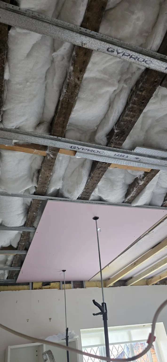 Kitchen ceiling during rebuilding, with exposed joists, insulation and metal support channels beside new plasterboard.