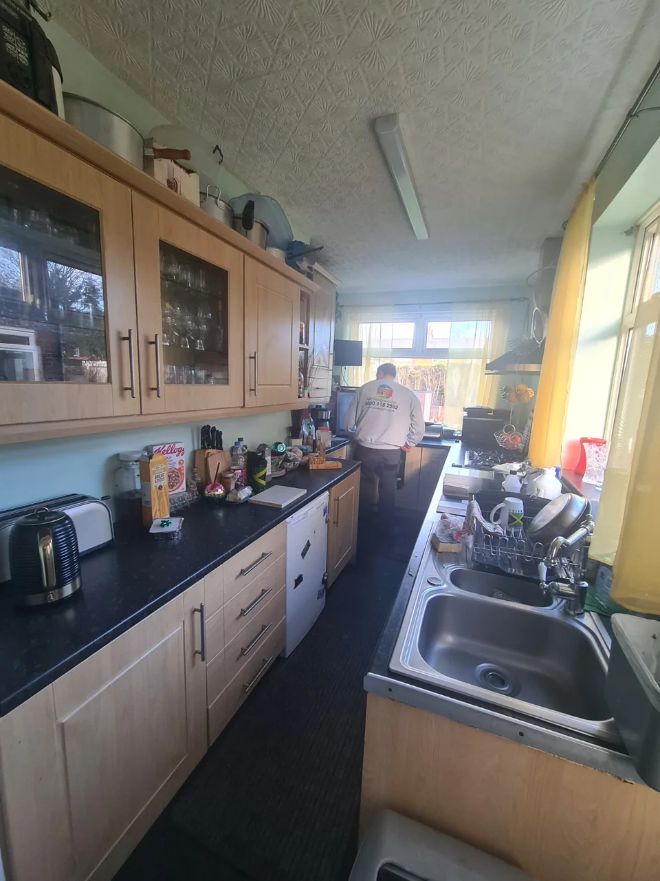 The original galley kitchen near Burnage, with wood-effect cabinets and a textured ceiling.