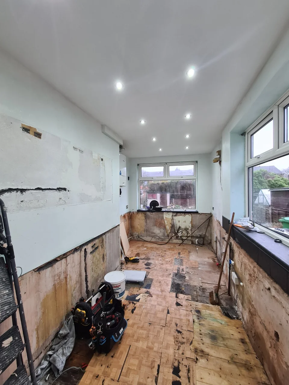 The Burnage kitchen with the old units removed, exposed floor and walls, and a smooth ceiling with recessed lights.