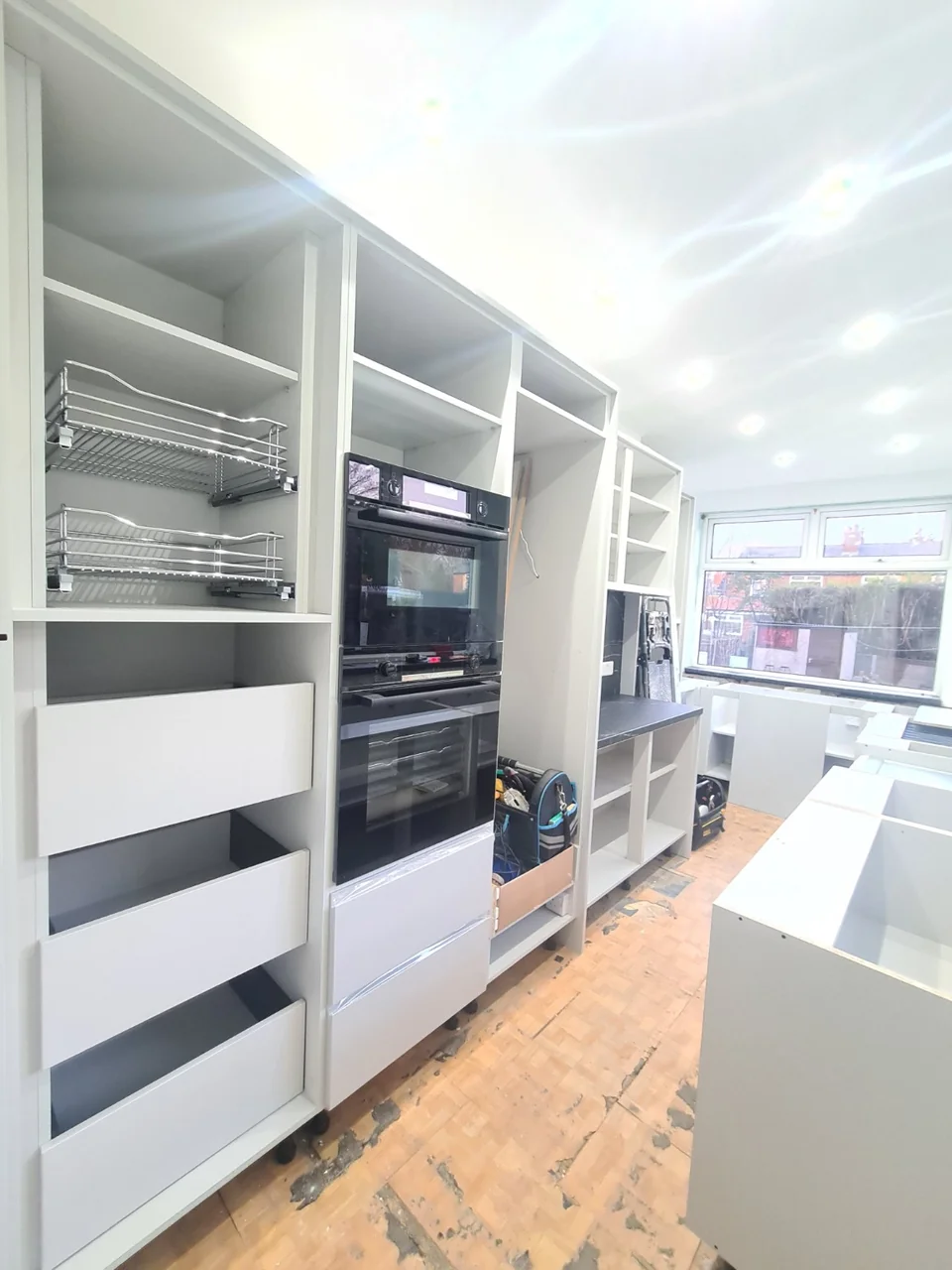 Tall kitchen cabinets with built-in ovens, storage baskets and drawers during fitting near Burnage.