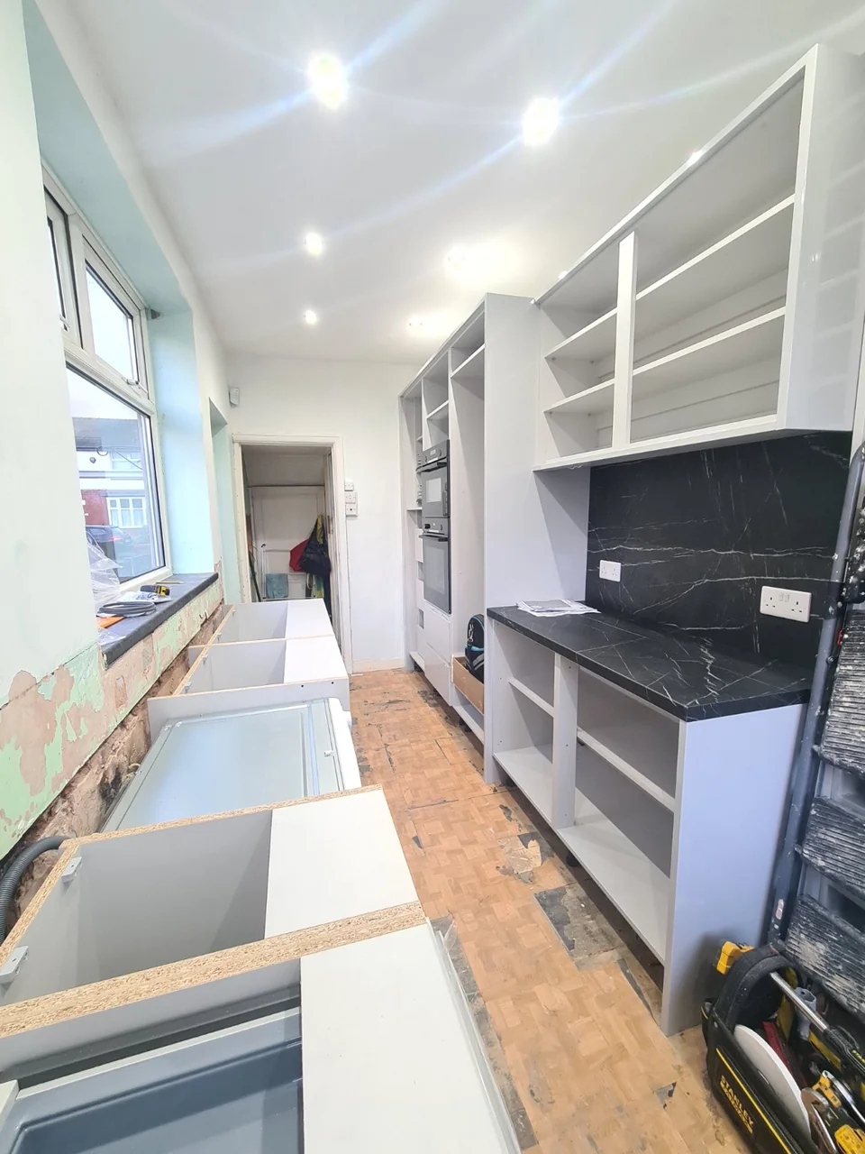 New kitchen cabinets and a dark veined worktop and splashback during installation near Burnage.