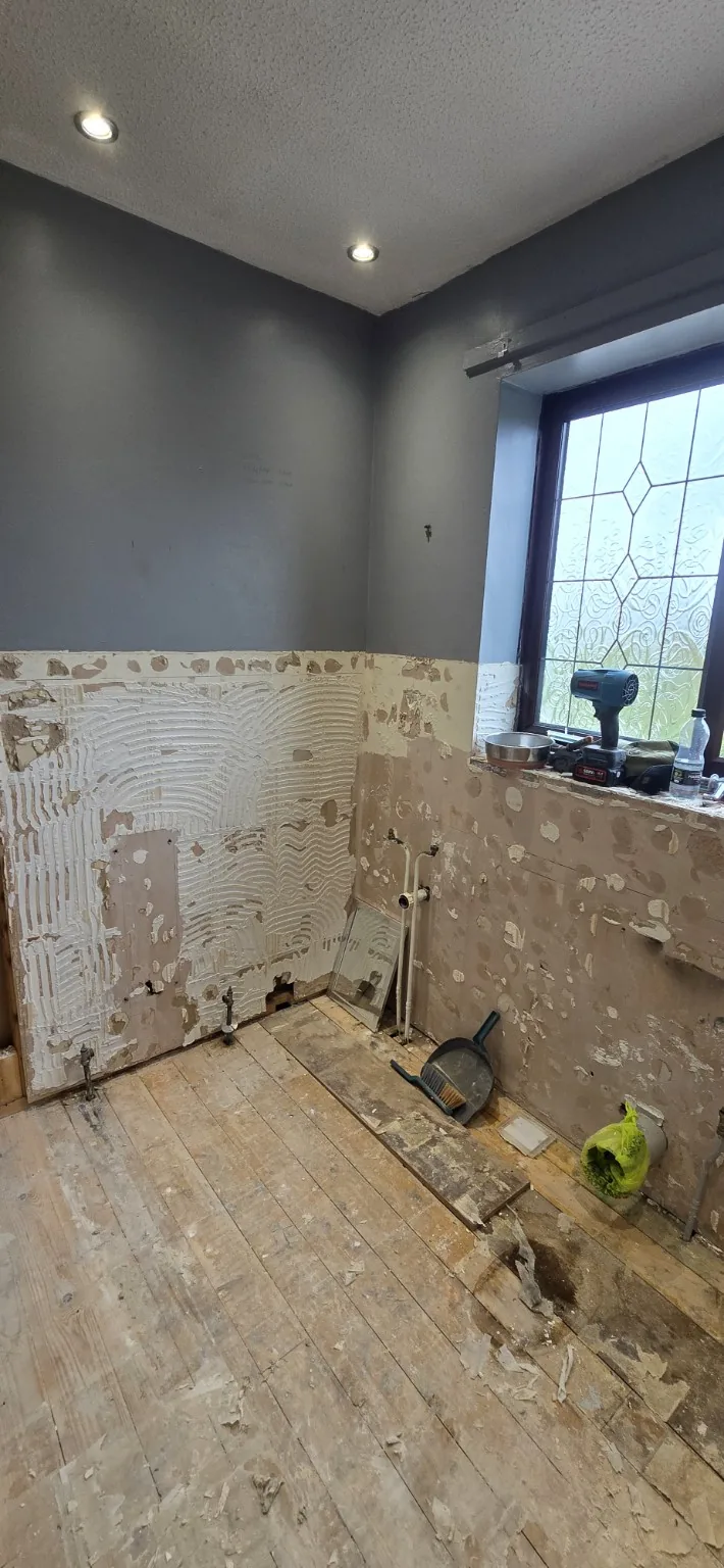 Bathroom with fittings and wall tiles removed, exposing floorboards and the lower wall surfaces.