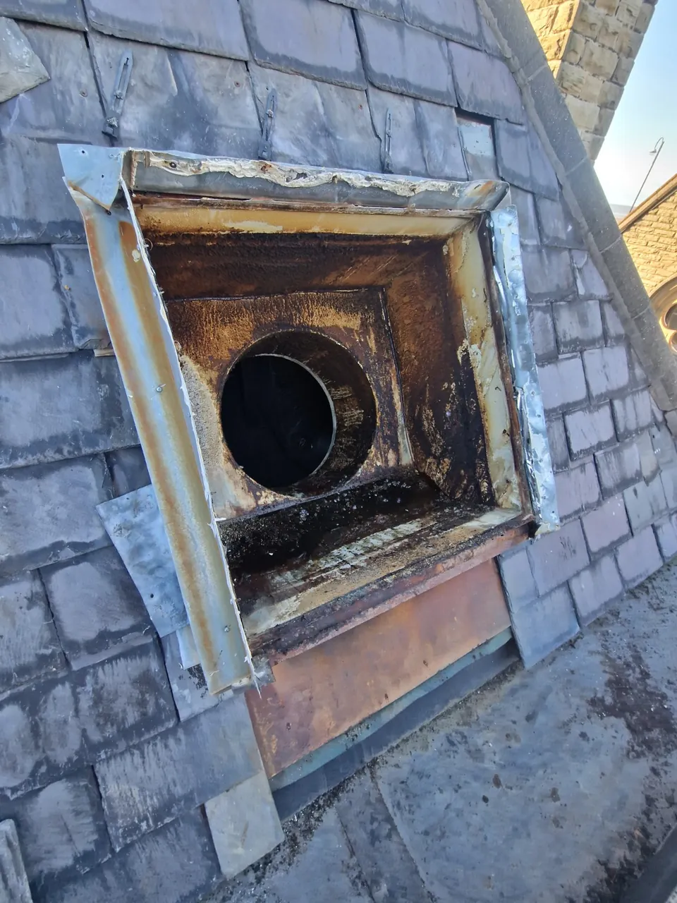 Old roof-mounted extractor housing with visible corrosion and a circular duct opening.
