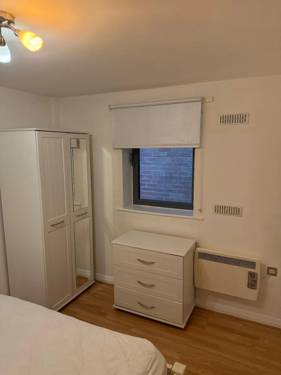 Reinstated Manchester bedroom with a decorated white wall, window blind, ventilation grilles and furniture back in place.