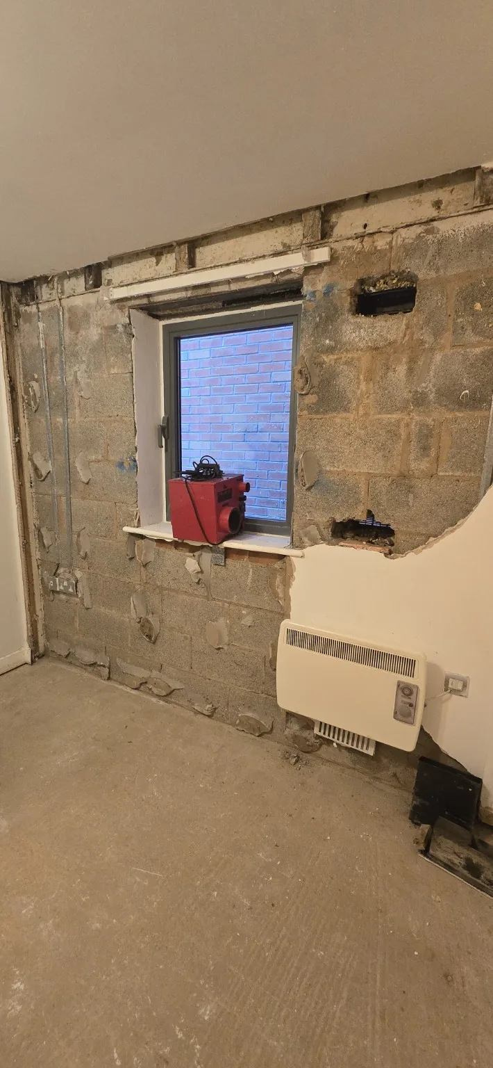 Bedroom wall stripped back around the window, exposing blockwork before reinstatement.