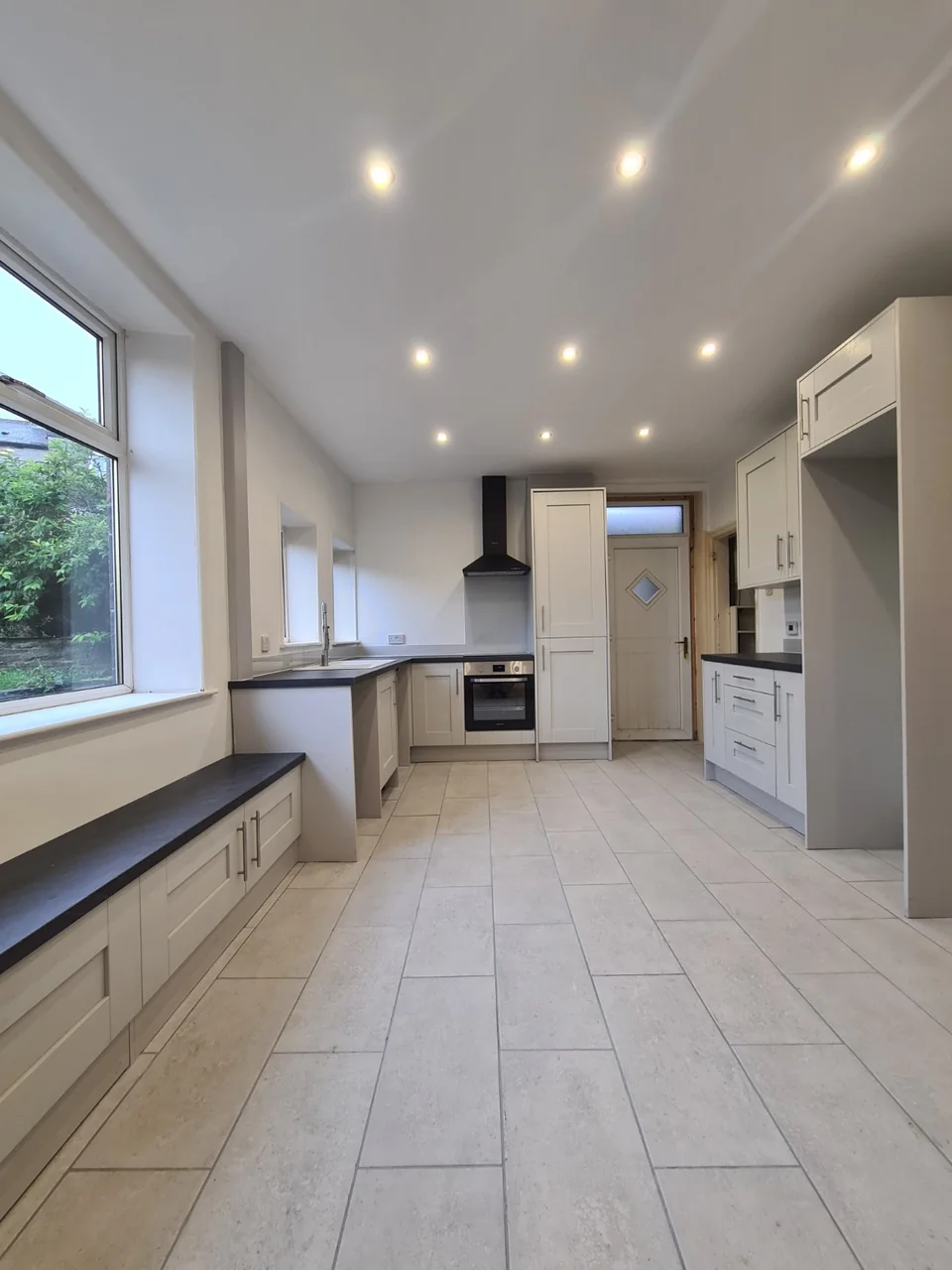 The enlarged Rawtenstall kitchen with pale shaker-style cabinets, dark worktops and a tiled floor.