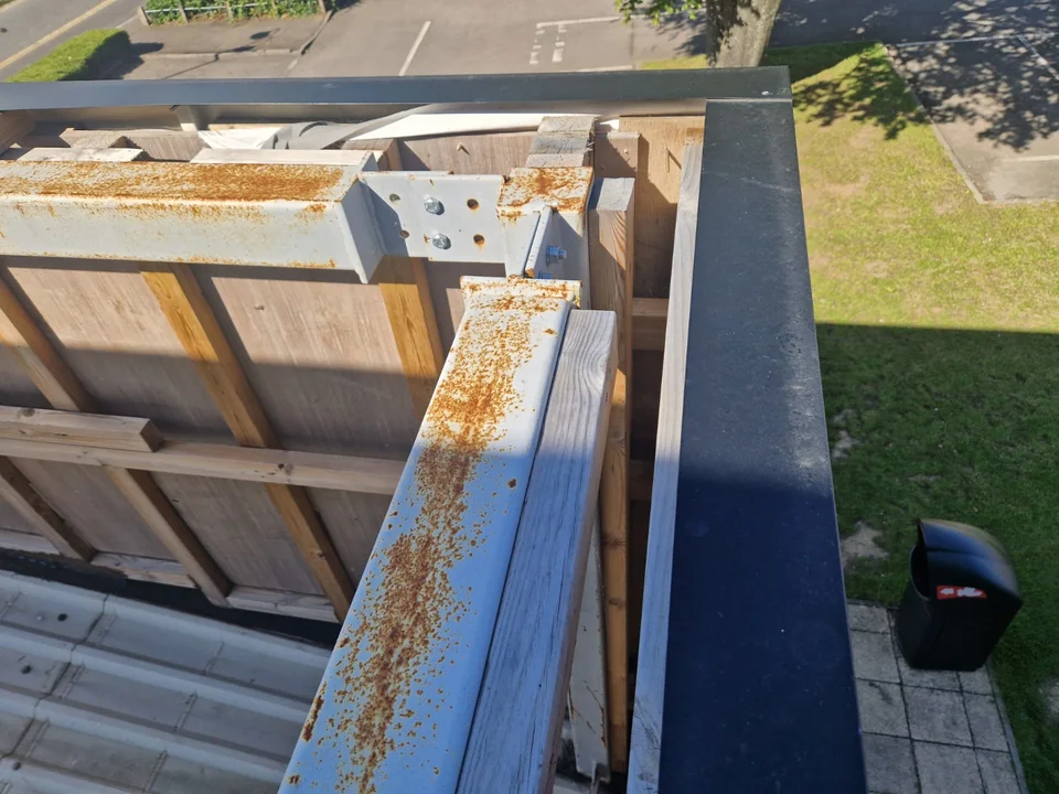 Close view of roof-edge metal supports, timber framing and dark perimeter capping.