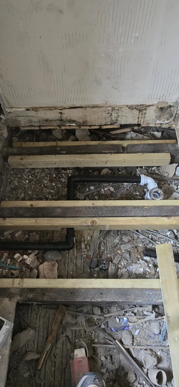 Exposed bathroom floor with new timber reinforcement and shower waste pipework.