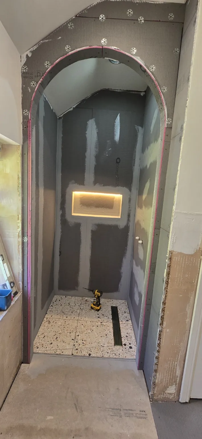 Boarded arched shower enclosure with sealed joints, an illuminated niche and partially laid floor tiles.